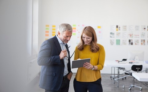 Male and female professional smiling and looking at a tablet device